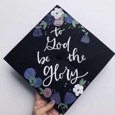 a hand holding a graduation cap that says to god be the glory