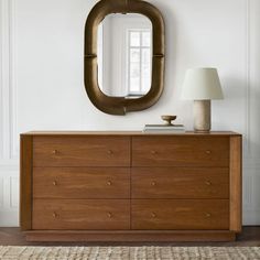 a wooden dresser with a mirror above it and a lamp on top of the dresser