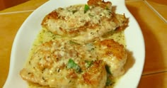 two pieces of meat covered in sauce on a white plate next to a brown tile floor