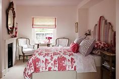 a bedroom with pink walls and bedding in the corner, chairs are on either side of the window