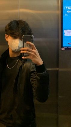 a man wearing a face mask while looking at his cell phone in front of an elevator