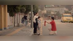 a man kneeling down next to a woman holding a red tie on the side of a road