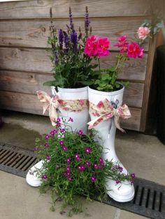 two white boots with flowers in them sitting on the ground next to a drain grate