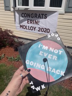 a hand holding up a graduation cap with congratulationss on it and an i'm not ever going back sign