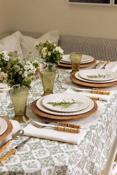 the table is set with place settings and flowers in vases on top of it