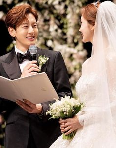 a bride and groom holding a microphone during their wedding ceremony at the same time as they stand next to each other