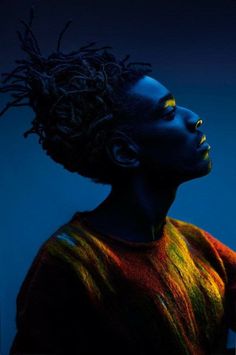 a woman with dreadlocks standing in front of a blue background and looking off to the side