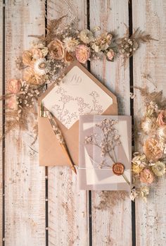 the wedding stationery is laid out on top of the wooden table with dried flowers