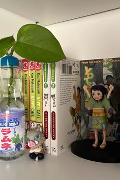 an open book next to a plastic toy and some books on a table with a plant