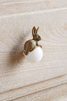 a golden rabbit head mounted on the side of a white dresser drawer with an egg in it's mouth