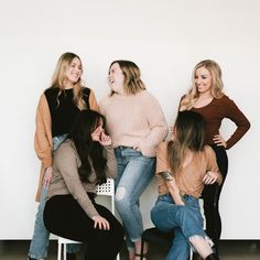 four women are posing for the camera in front of a white wall and one woman is sitting on a chair