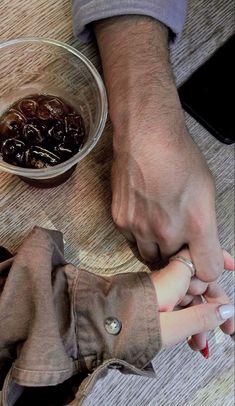 a man and woman holding hands over a bowl of food on a wooden table next to a cell phone