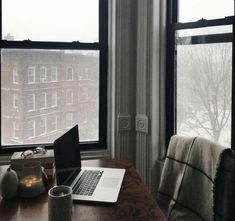 an open laptop computer sitting on top of a wooden desk next to a large window