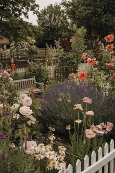 a garden filled with lots of flowers next to a white picket fence and wooden bench