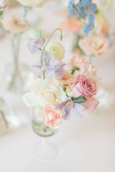 there are many small vases with flowers in them on the tableclothed table