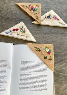 an open book sitting on top of a wooden table next to three pieces of embroidered fabric