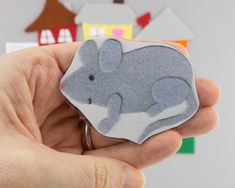 a hand holding a small gray and white elephant brooch with houses in the background