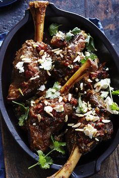 a pan filled with meat and vegetables on top of a wooden table next to utensils