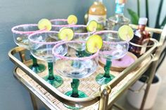 there are many glasses that have lemons in them on the tray with bottles behind it