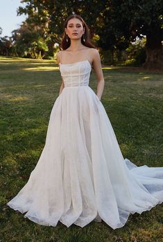 a woman standing in the grass wearing a wedding dress