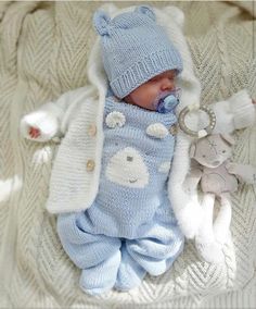 a baby laying on top of a blanket wearing a blue outfit and hat with a pacifier in it's mouth