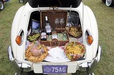 the back end of an old car with food and wine in it, including grapes