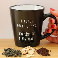 a woman holding a black coffee mug with white writing on it next to some dried herbs