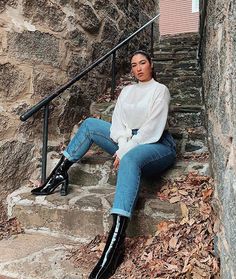 a woman is sitting on the steps wearing black boots and white shirt with blue jeans