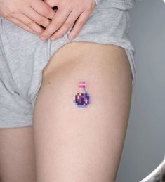 a person with a small tattoo on their thigh that has a pink and blue bottle in it