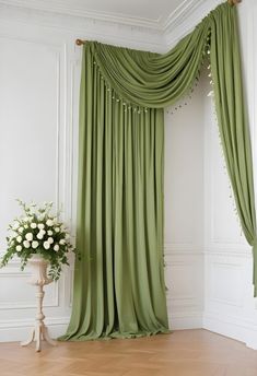 a green drapes in the corner of a room next to a vase with flowers