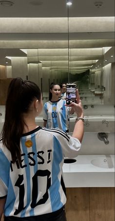 a woman taking a selfie in front of a bathroom mirror with her cell phone