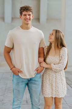 a young man and woman standing next to each other in front of a white building