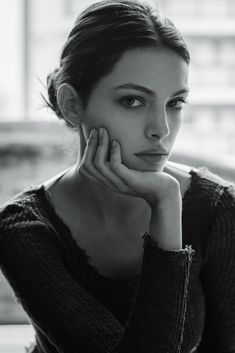 a black and white photo of a woman with her hand on her chin looking at the camera