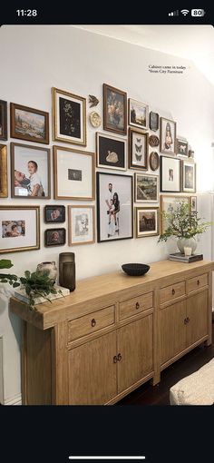 a large wooden dresser sitting in front of a wall filled with pictures and framed photos