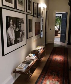 a long hallway with many framed pictures on the wall and an area rug in front of it