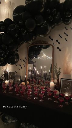 a table topped with lots of black balloons and candles next to a mirror filled with wine glasses