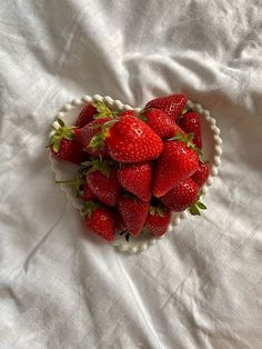 a heart shaped bowl filled with strawberries on top of a white sheet