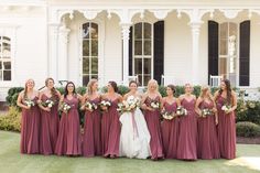 a group of women standing next to each other in front of a white building holding bouquets