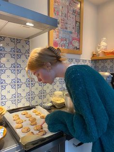 a woman in blue sweater baking cookies on top of an oven with cookie sheet next to her