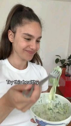 a girl is eating broccoli from a bowl with a spoon in her hand