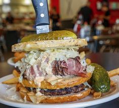 a large sandwich on top of a white plate with french fries and a knife sticking out of it