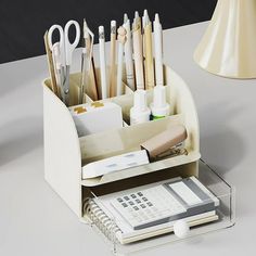 an organized desk with pens, pencils and other office supplies on the table next to a lamp