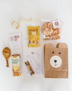 an assortment of snacks and treats laid out on a white surface with paper bags, scissors, pencils, markers, and other items