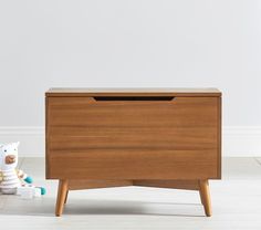 a wooden chest sitting on top of a white floor next to a stuffed animal toy