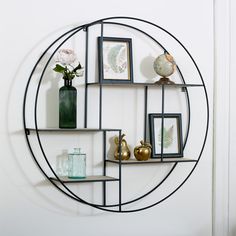 a round metal shelf with pictures and vases on it's sides in front of a white wall