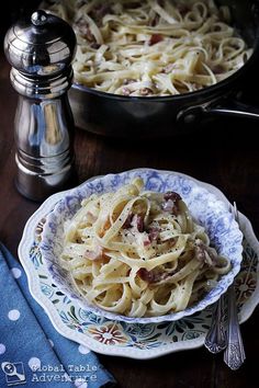 a bowl of pasta with bacon and parmesan cheese in it on a table