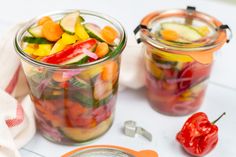 two glass jars filled with pickles and veggies next to a measuring spoon