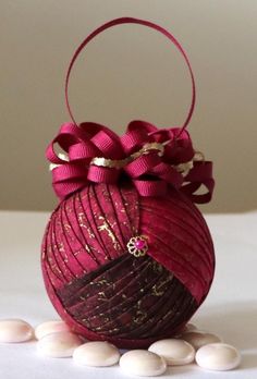 a red ornament sitting on top of some white rocks with a ribbon around it