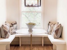 a white table with two benches and a bowl on it in front of a window