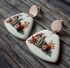 two white and gold earrings with flowers on them sitting on top of a wooden table